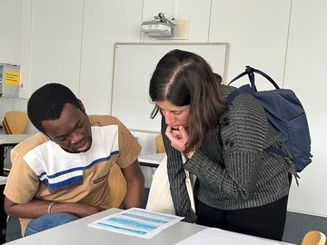 Zwei Studierende betrachten ein Arbeitsblatt auf einem Tisch.