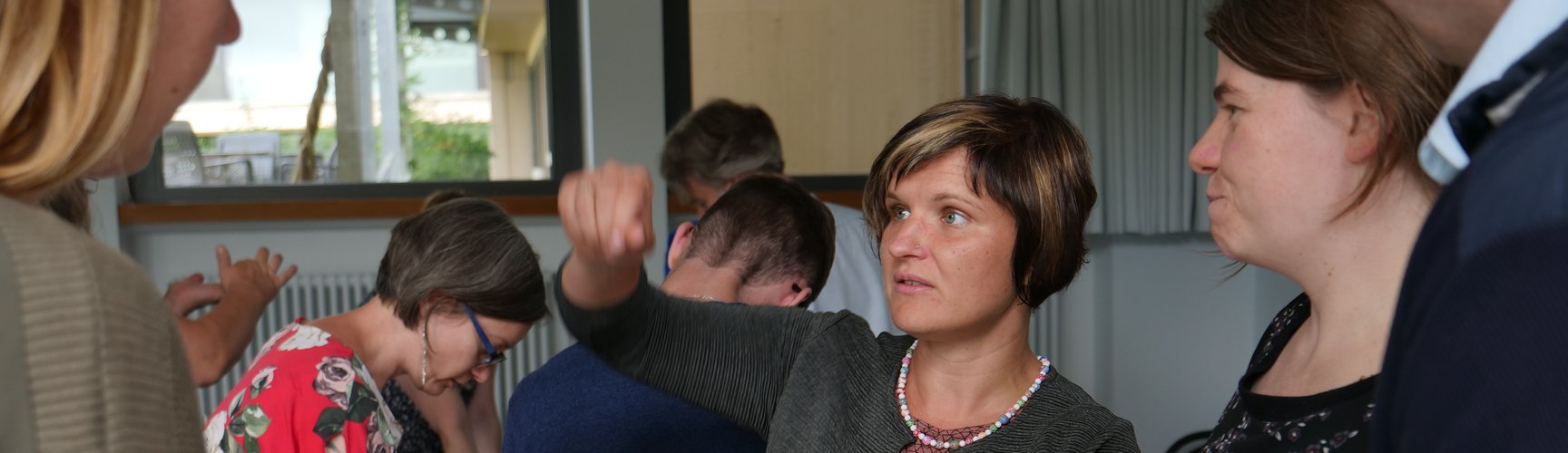 Drei Frauen unterhalten sich, im Hintergrund stehen weitere Personen um Tische herum.