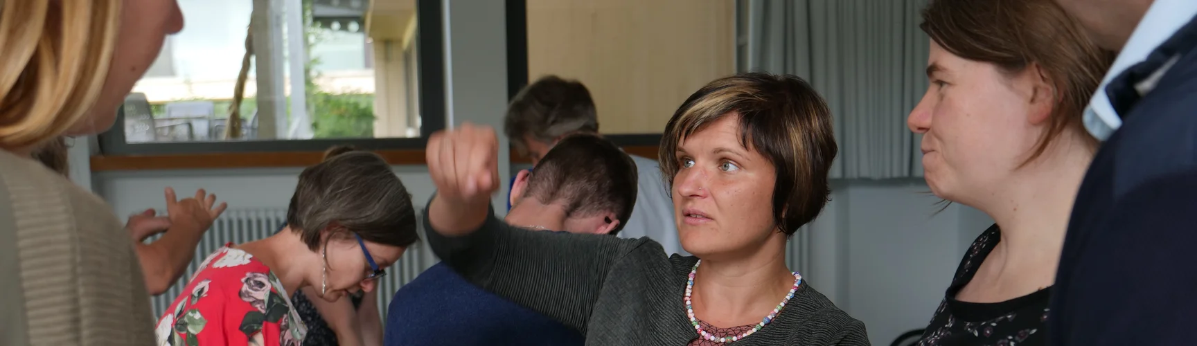 Drei Frauen unterhalten sich, im Hintergrund stehen weitere Personen um Tische herum.