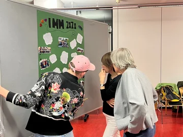 Drei Personen betrachten ein Poster mit dem Titel IMM 2020.