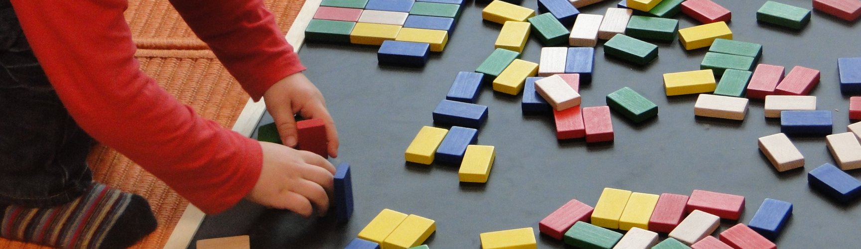 Ein Kind spielt auf dem Boden mit bunten Dominosteinen.