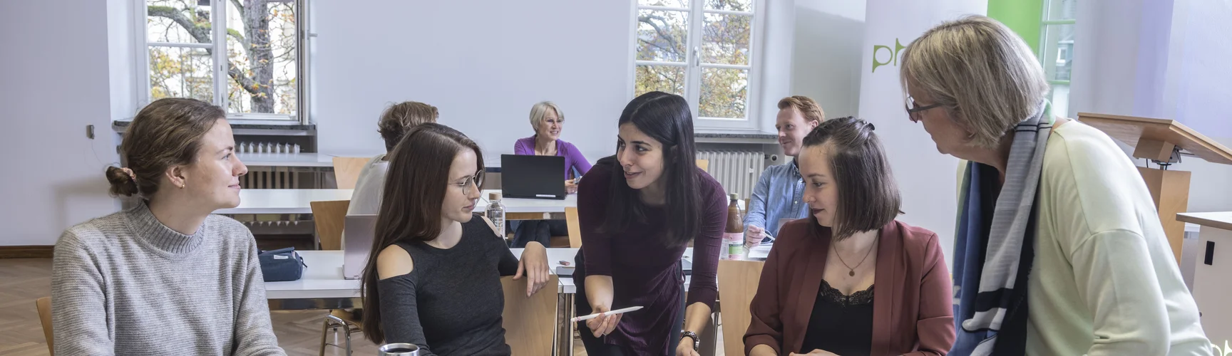 Studierende sitzen in einem Seminarraum in Tischreihen und besprechen sich.