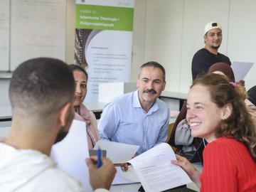 Mehrere Personen sitzen in einem Seminarraum um einen Tisch und halten Blätter in der Hand.