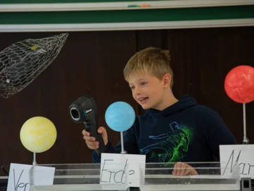 Junge hält ein Infrarotthermometer auf ein Modell der Venus.