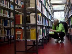 Ein Student sucht ein Buch in einem Bücherregal der Hochschulbibliothek