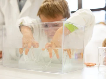 Ein Junge in Laborkittel experimentiert mit Gefäßen in einem Wassertank auf einem Labortisch.