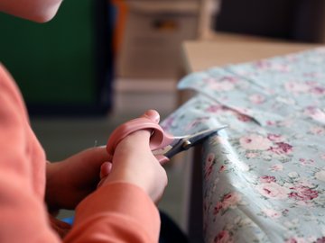 Ein KiTa-Kind sitzt an einem Tisch und schneidet mit einer Schere in ein Stück geblümten Stoff zu