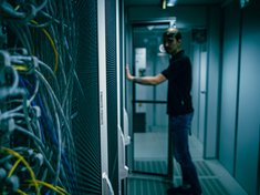 Ein Mann steht in einem Serverraum vor einem Schrank mit vielen Kabeln