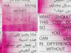 Typografisches Kunstwerk an einer Betonwand, bestehend aus mehrsprachigen Texttafeln in Rot-Weiß. Die Tafeln zeigen die Frage: „Was muss diese Stadt tun, damit du ohne Angst verschieden leben kannst?“ in mehreren Sprachen.