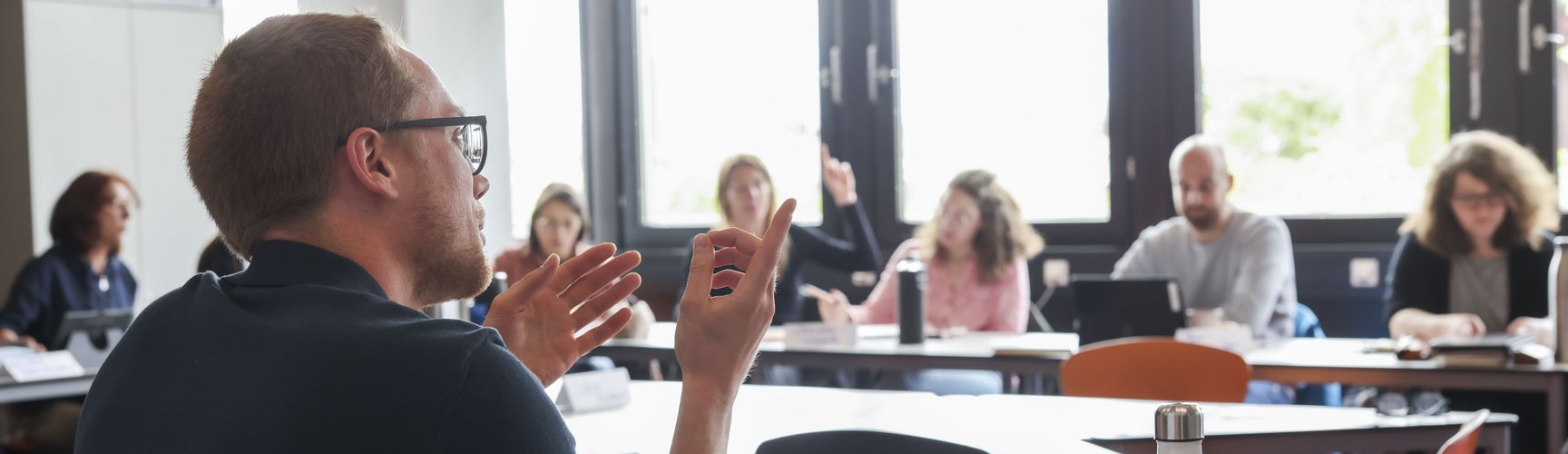 Szene aus einer Weiterbildungsveranstaltung: Personen sitzen in einer Runde und diskutieren, ein Mann im Vordergrund spricht gerade