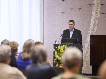 Prof. Weihs am Stehpult vor Publikum von hinten im Bürgersaal im Rathaus am Marktplatz.