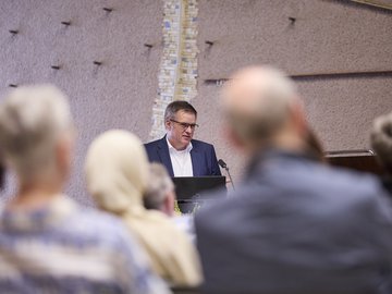 Durch Publikumsköpfe von hinten nindurch ist Prof. Gleser bei seinem Vortrag im Bürgersaal bei PHKA im Rathaus zu sehen.