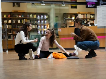 Eine Studentin sitzt in einem Museumsfoyer auf dem Boden, zwei weitere neben ihr in der Hocke.