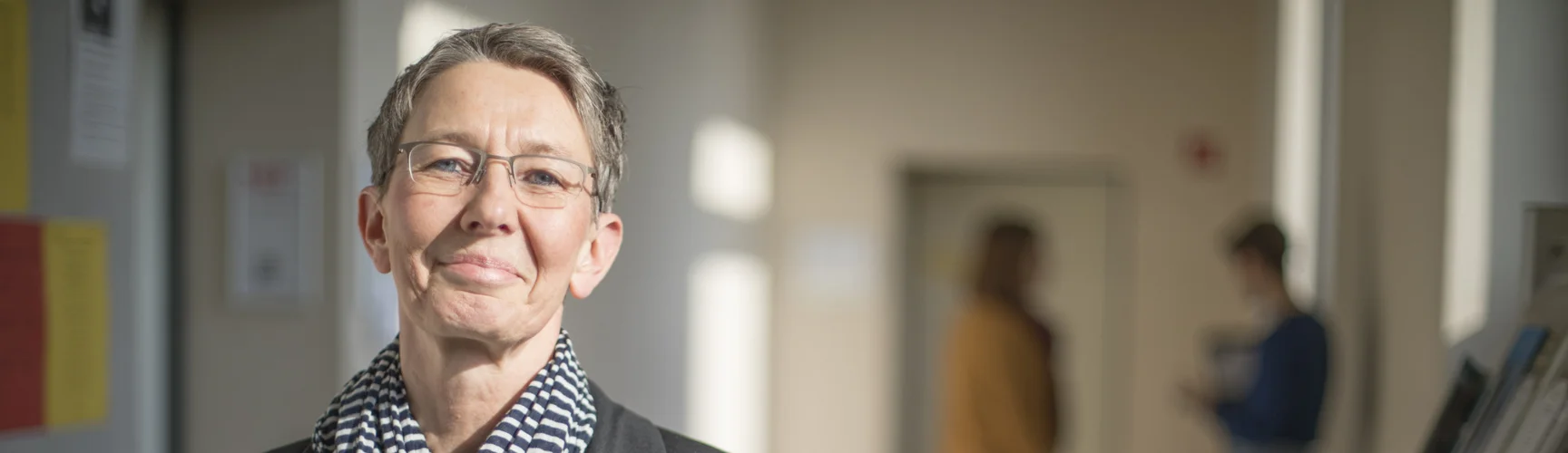 Eine Frau steht in einem Gang der Hochschule und hält ein Buch mit dem Titel "Selbstbestimmt lernen".