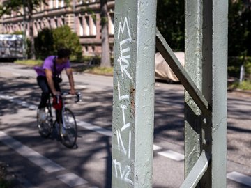 Pfosten mit Graffiti, im Hintergrund ein Radfahrer auf einem Rennrad