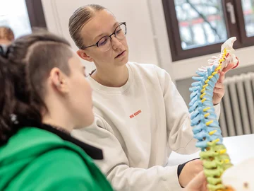zwei Studentinnen untersuchen eine künstliche Wirbelsäule