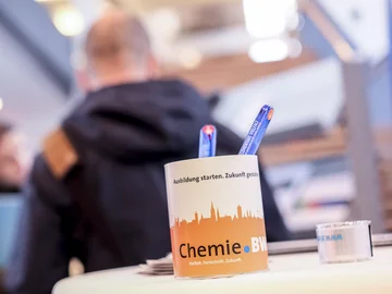 Nahaufnahme einer Tasse mit Chemie-BW-Logo. Menschen im Hintergrund.