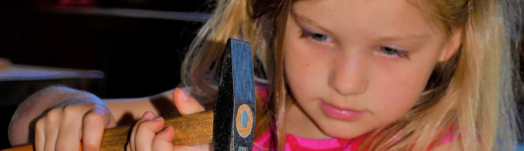 Ein Kindergartenkind schlägt mit einem Hammer einen Nagel ein