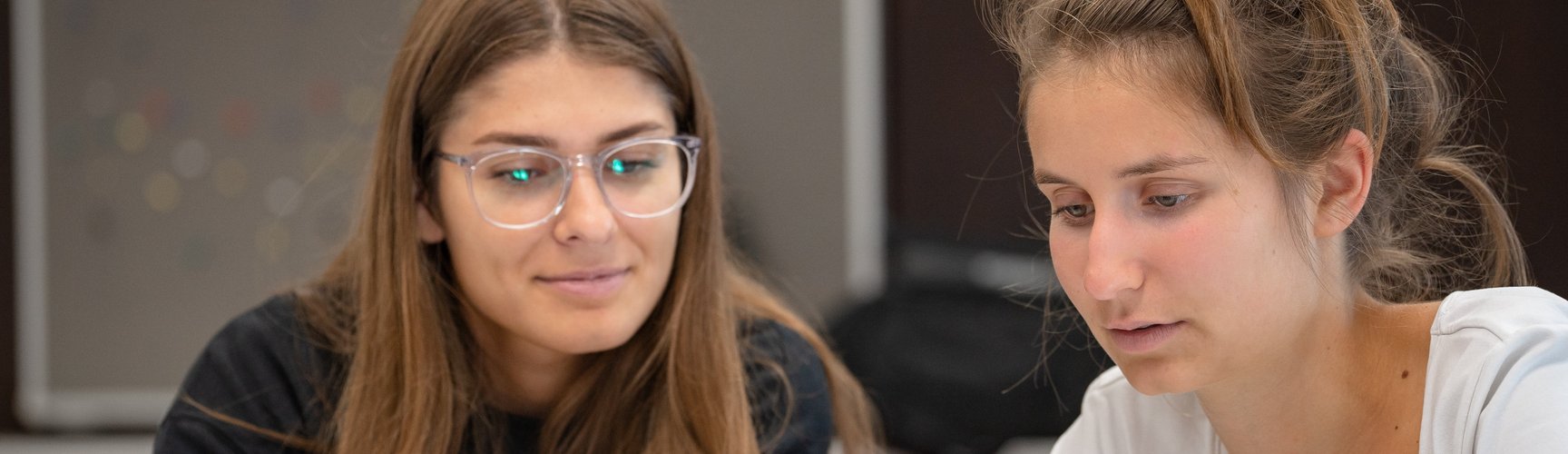 Zwei Studentinnen in einem Seminarraum blicken gemeinsam auf ein Tablet.