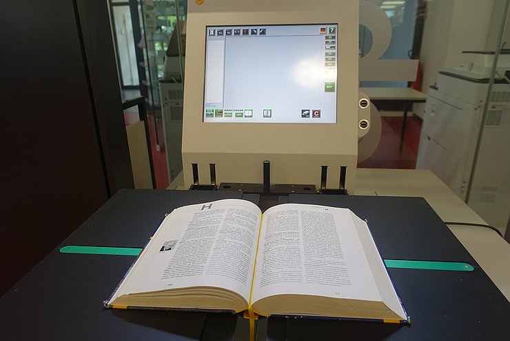 Man sieht ein aufgeschlagenes Buch auf einem Buchscanner liegen.