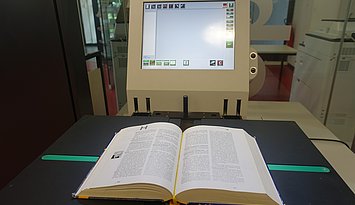 Buchscanner Man sieht ein aufgeschlagenes Buch auf einem Buchscanner liegen.