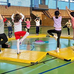 In eienr Sporthalle machen Kinder auf Matten Streck- und Balanceübungen