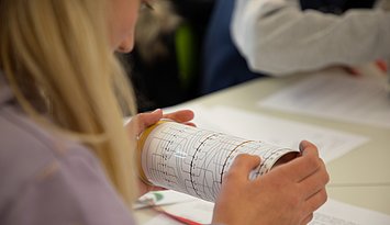 Eien Schülerin von hinten, die konzentriert auf bildlich dargestellte Programmierschritte auf einer Rolle blickt.