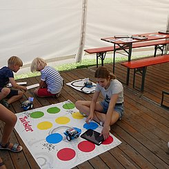 PHKA Lehr-Lern-Labor Informatik bei EFFEKTE 2023 Blick in das Pagodenzelt des Lehr-Lern-Labors Informatik bei EFFEKTE 2023. Im Hintergrund eine Biertischgarnitur mit Tablets und Unterlagen, vorne Kinder platziert um eine Twisterfolie mit mBots und Tablets