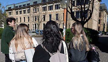 Drei Studentinnen und ein Student von hinten vor dem Gebäude 3 im Herbst