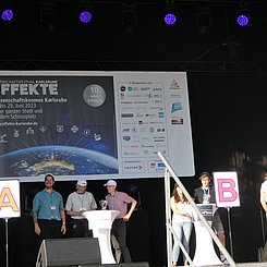 "Duell der klugen Köpfe" mit PHKA Beteiligung bei EFFEKTE 2023 Moderator und Kandidat:innen des Quiz "Geistesblitze - Duell der klugen Köpfe" auf der EFFEKTE-Event-Bühne. Es sind die Stationen A und B zu sehen. Rechts vom A steht Jun.Prof. Dr. Sebastian Engelmann, rechts vom B eine PHKA Lehramtsstudentin. Im Hintergrund ist das EFFEKTE Bahner aufgespannt mit dem Plakatmotiv und den Logos aller beteiligten Institutionen.